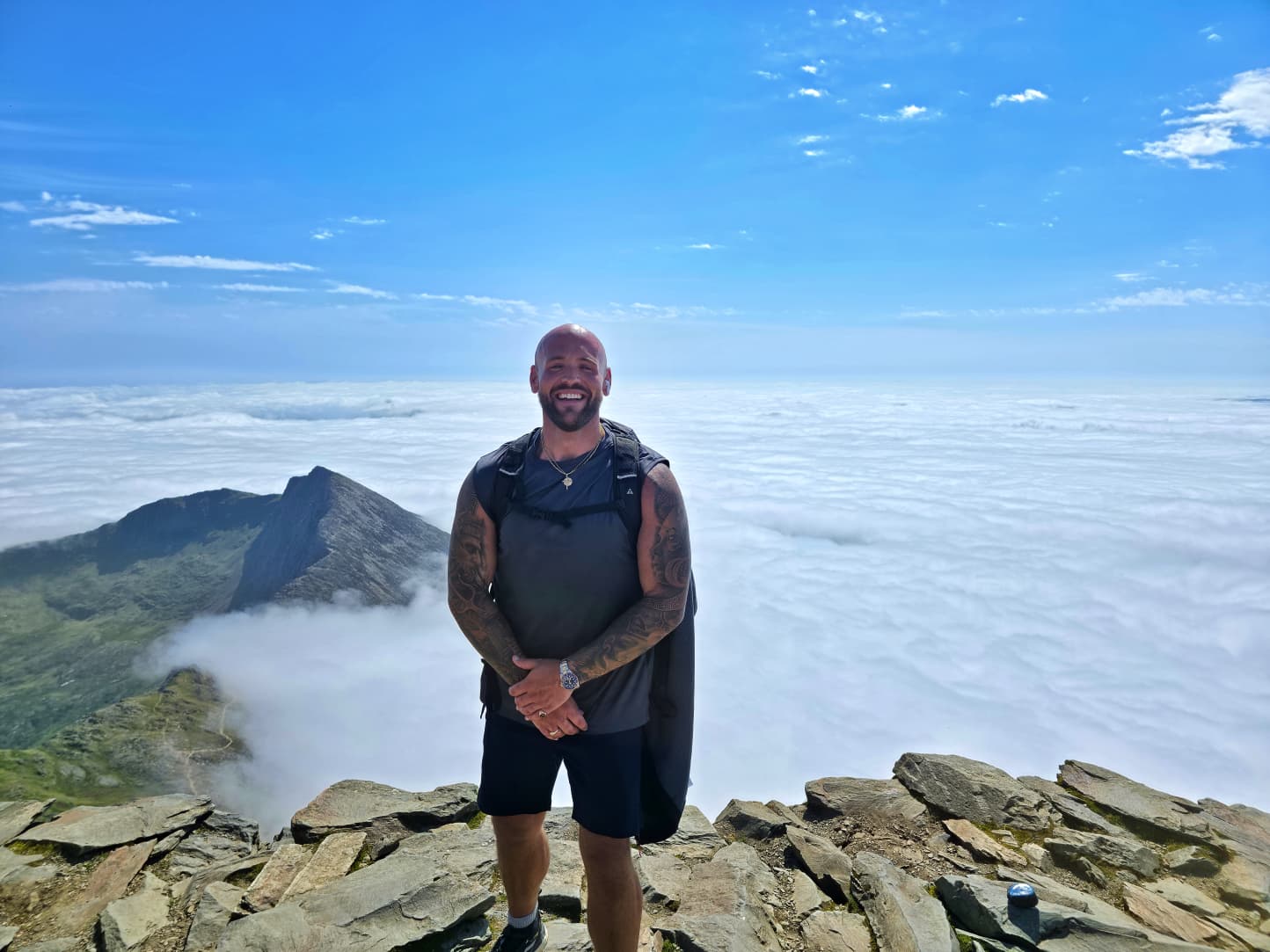 Jeff Charles smiling on a mountain summit above the clouds